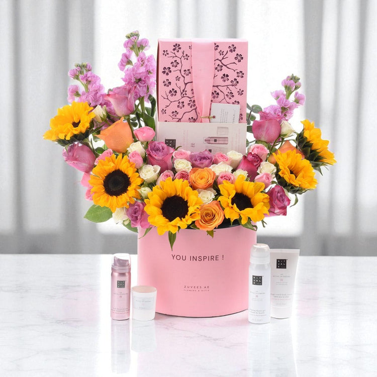 Pink box holds vibrant sunflowers, roses, and blooms with matching skincare set.
