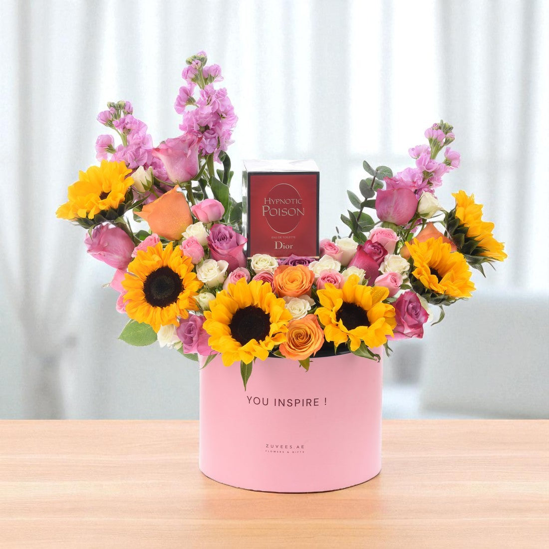 Vibrant sunflowers, roses, and snapdragons in pink box with "YOU INSPIRE!" and Dior perfume.