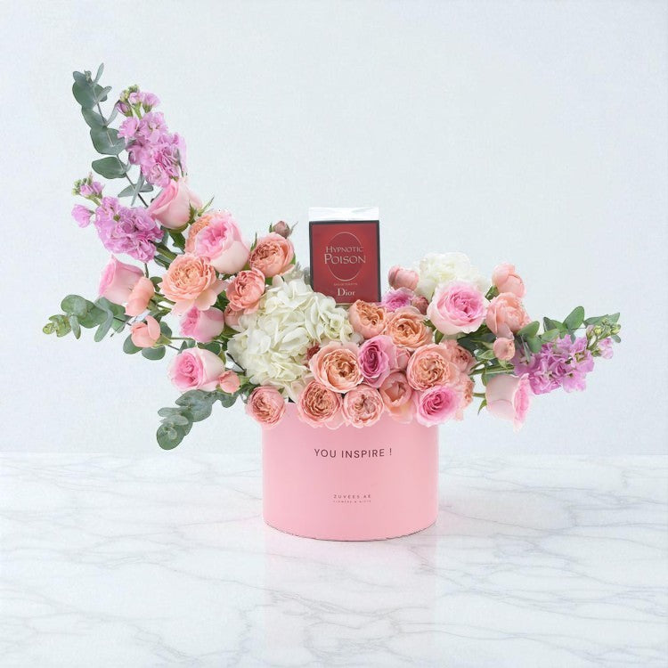 Pink floral arrangement with Dior perfume in branded box on marble.