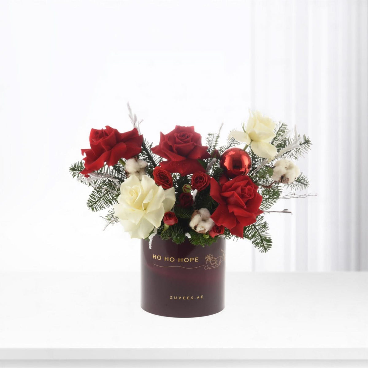 Red and white roses, pine, cotton, and ornament in festive dark vase.