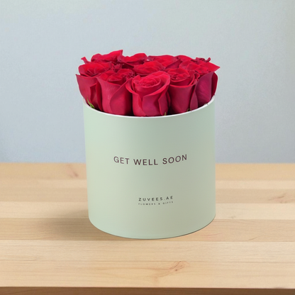 Vibrant red roses in mint-green box reading "Get Well Soon" on wooden surface.