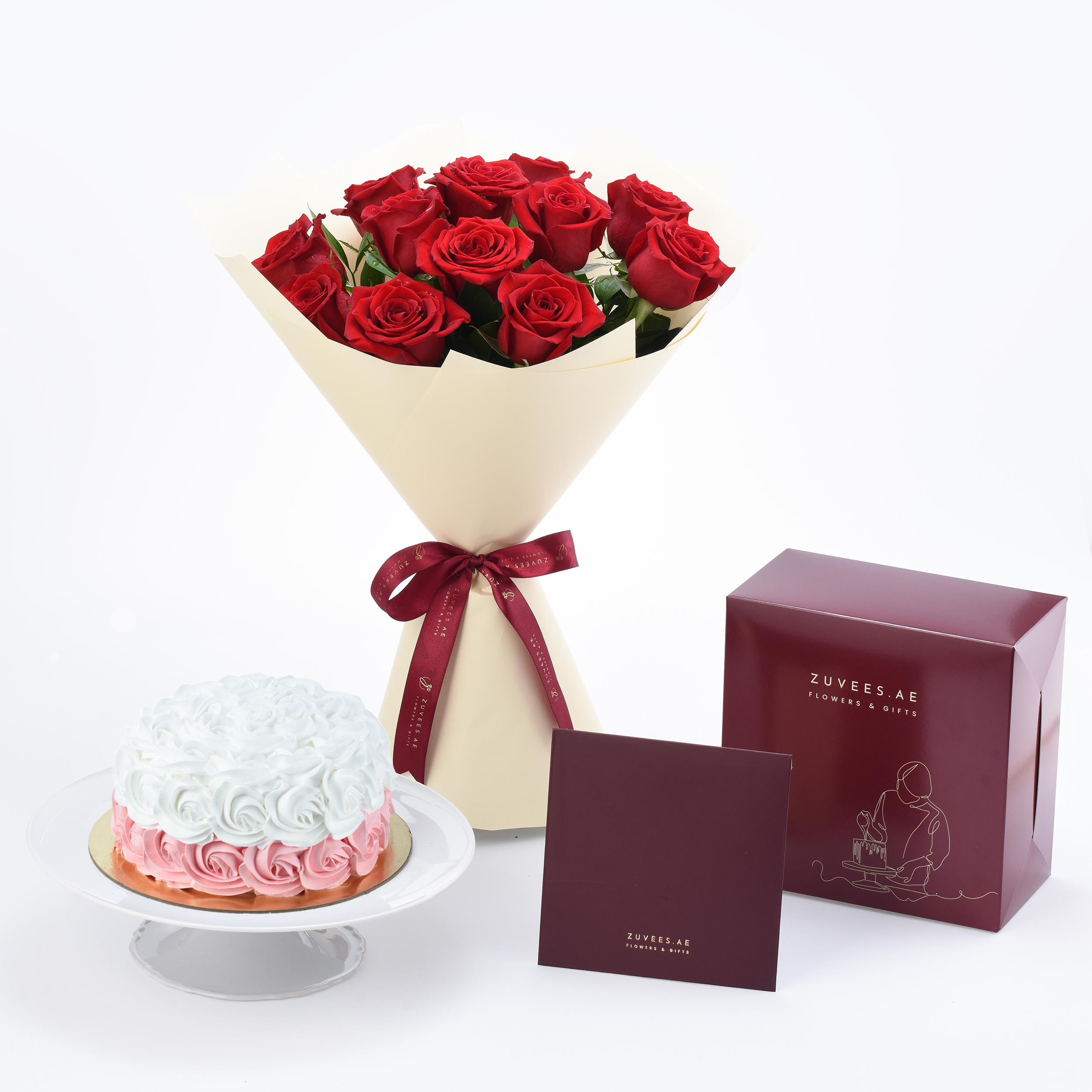 Vibrant red roses in cream wrap with burgundy bow, paired with pink-white cake and branded gift box.