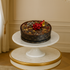 Luxurious fruitcake adorned with red bow, silver star, and gold bell on marble pedestal.