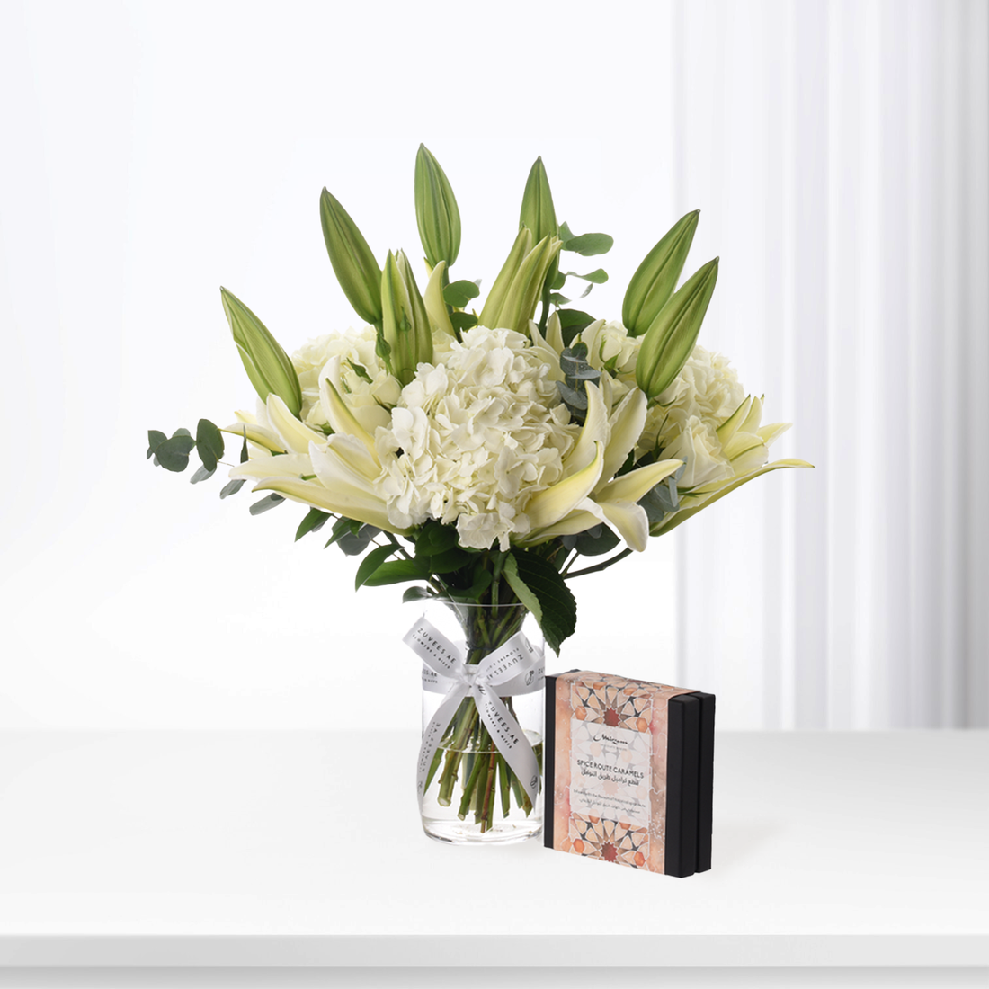 Elegant white lilies and hydrangeas in glass vase with caramel gift box.