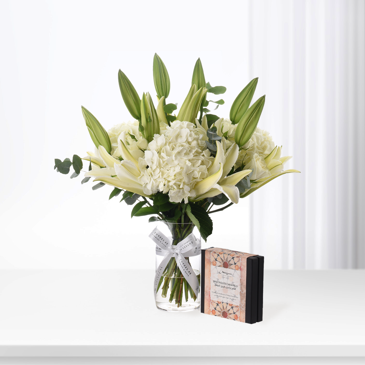 Elegant white lilies and hydrangeas in glass vase with caramel gift box.