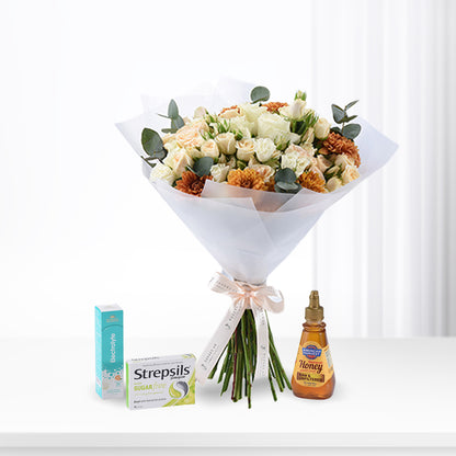 White roses and orange carnations wrapped in sheer paper, with Strepsils, honey, and electrolyte beside.