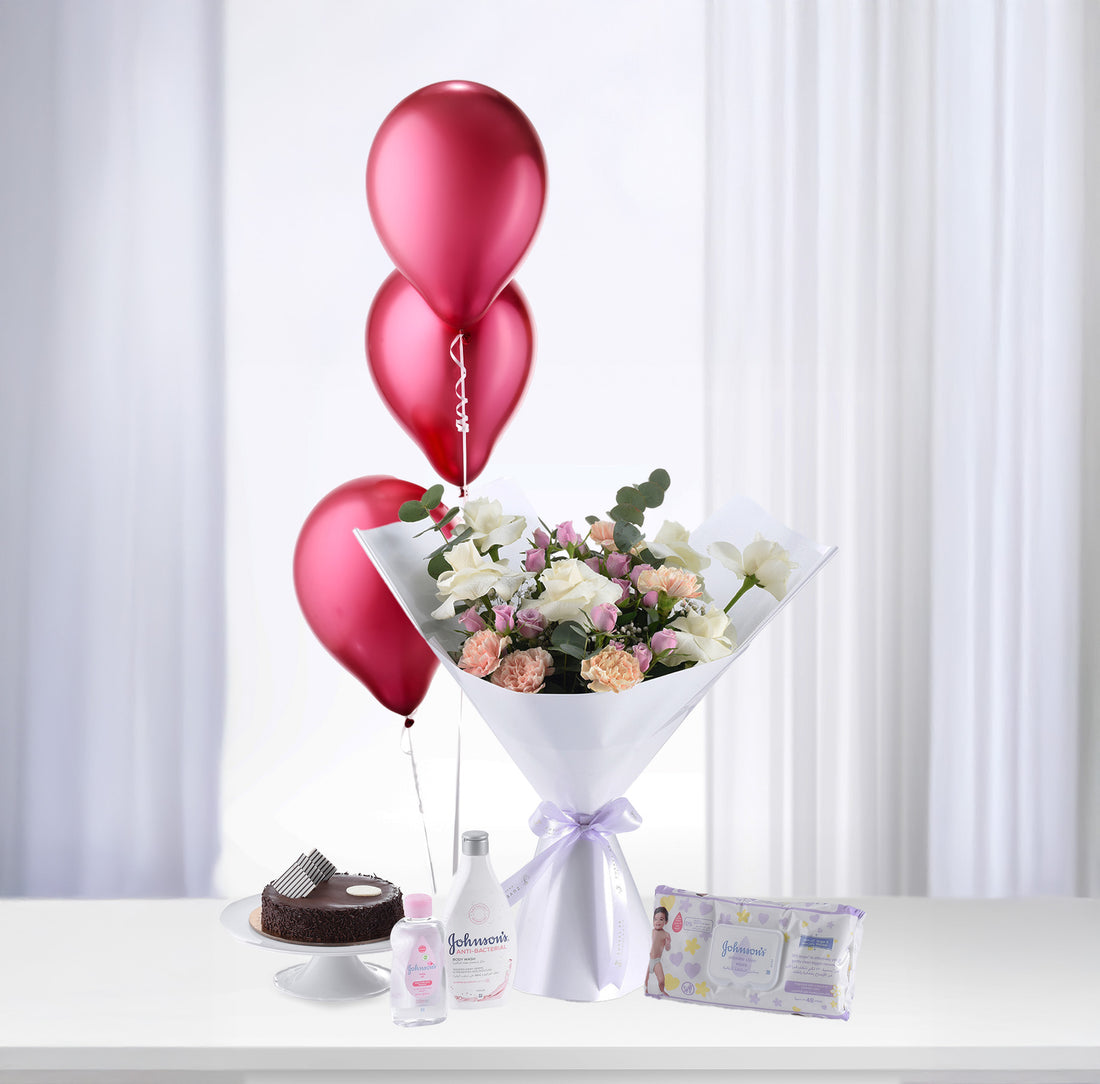 Pink balloons rise above white-wrapped floral bouquet beside baby care products and chocolate cake.