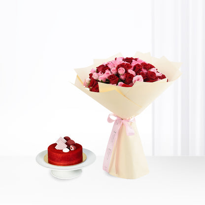 Vibrant red and pink roses bouquet with cream wrap, beside red velvet cake on stand.