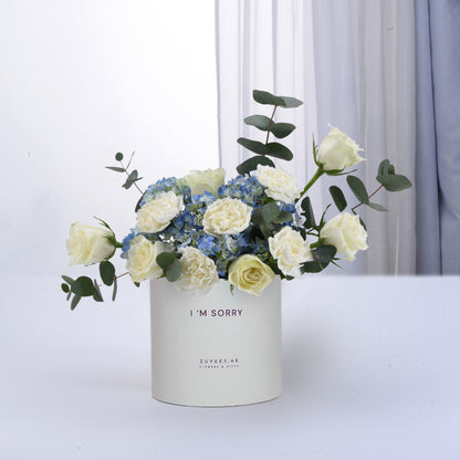 White roses and blue hydrangeas in minimalist white box with "I&