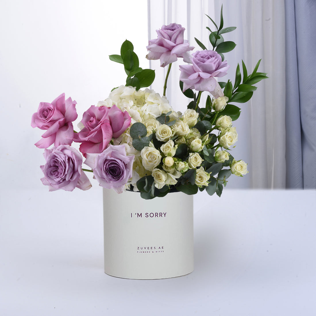 Pastel purple, pink, and white roses with greenery in minimalist white vase labeled "I&