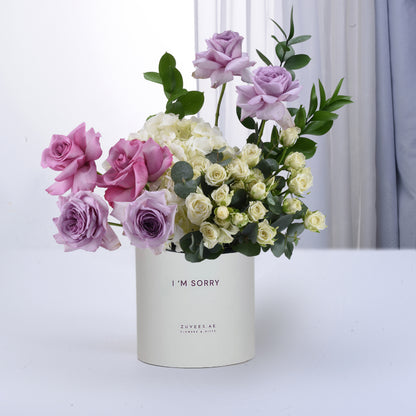 Pastel purple, pink, and white roses with greenery in minimalist white vase labeled "I&