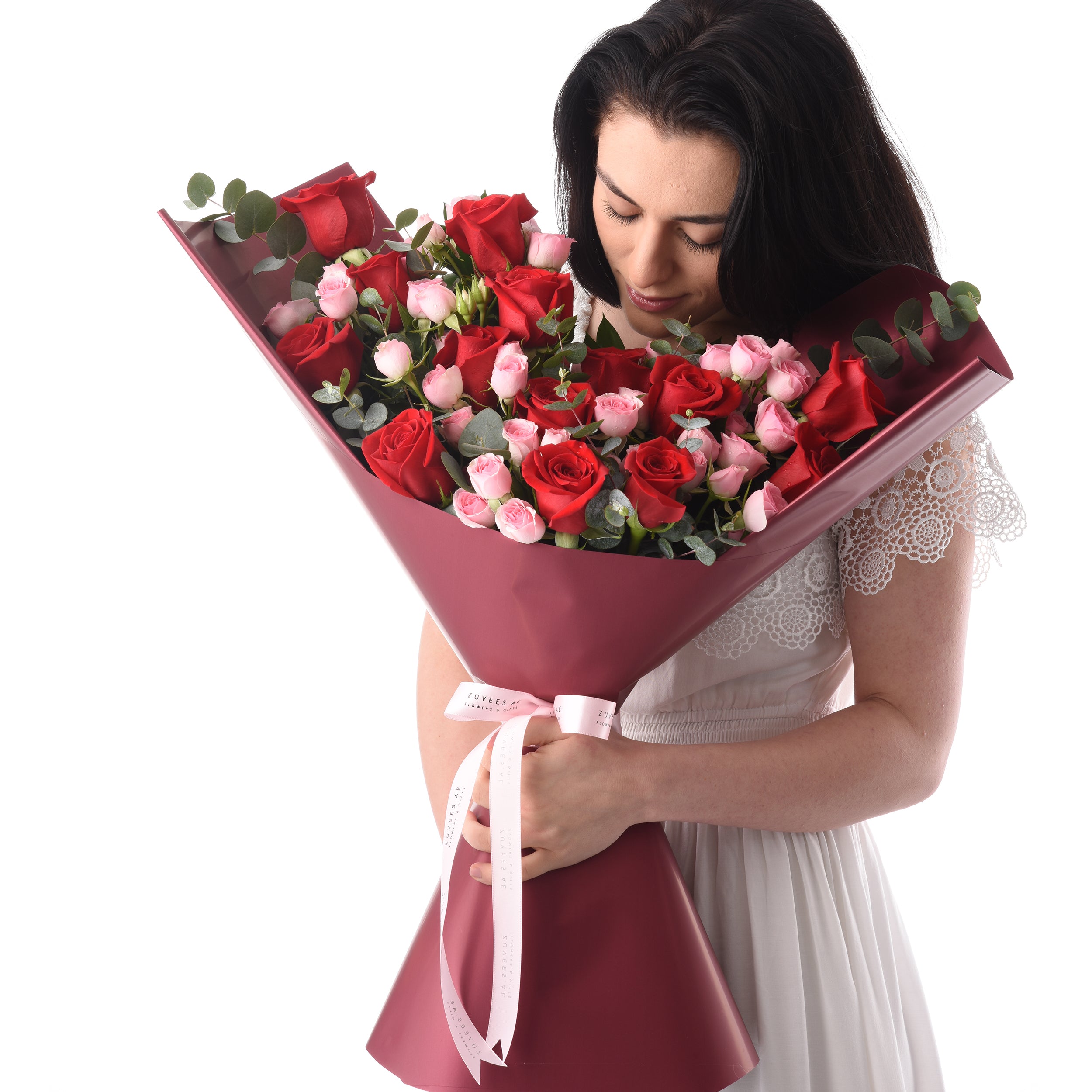 Woman cradles vibrant red and pink rose bouquet wrapped in burgundy paper.