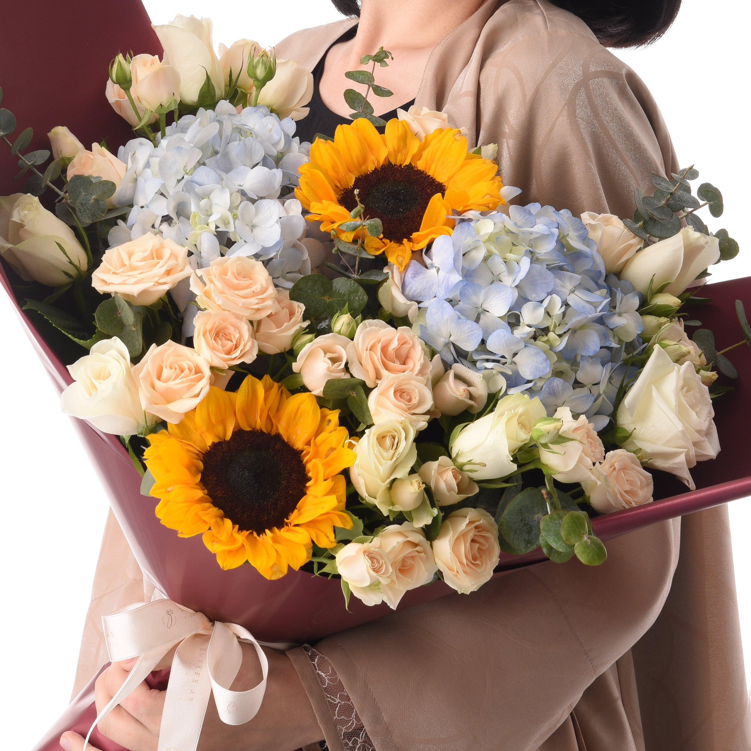 Vibrant sunflowers, blush roses, and blue hydrangeas in burgundy wrap.