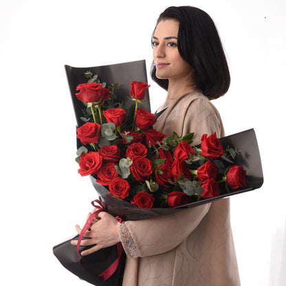 Woman holds lush red rose bouquet wrapped in sleek black paper with burgundy ribbon.