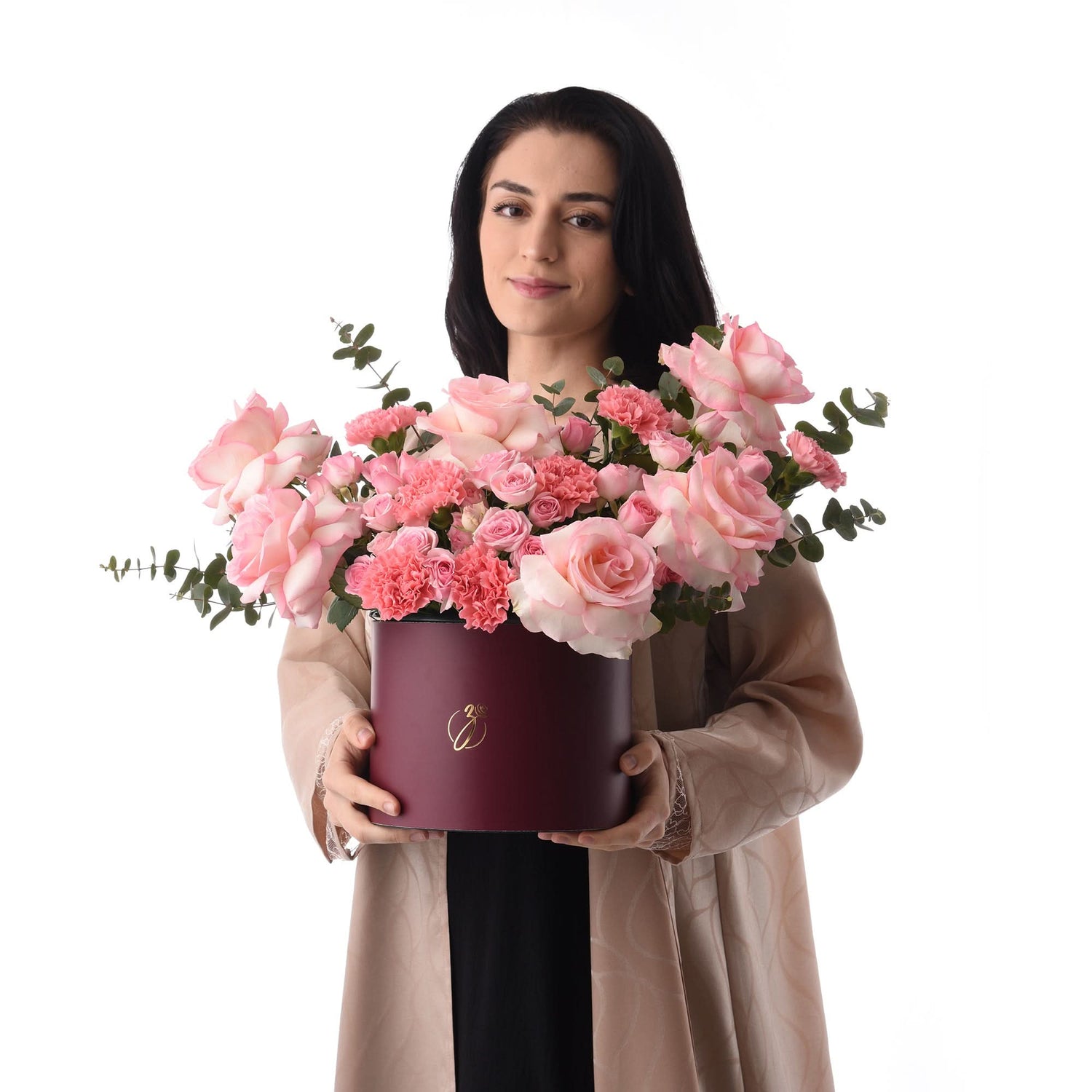 Woman holds burgundy box overflowing with soft pink roses and carnations.