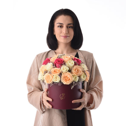 Woman holds burgundy hat box filled with vibrant peach, pink, and cream roses.