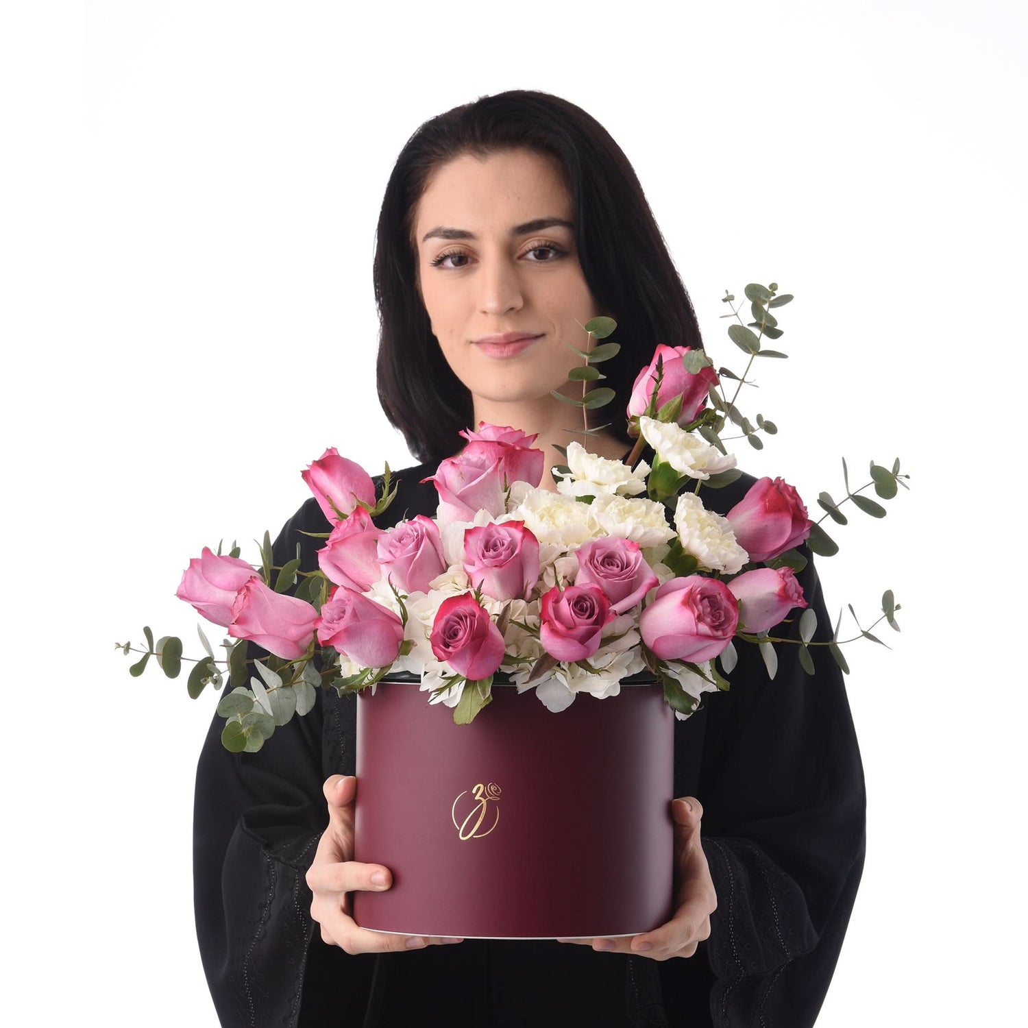 Woman holds burgundy hat box overflowing with pink roses and white blooms.
