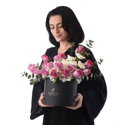 Woman holds elegant black box with pink roses, white blooms, and eucalyptus, branded Zuvees.ae.