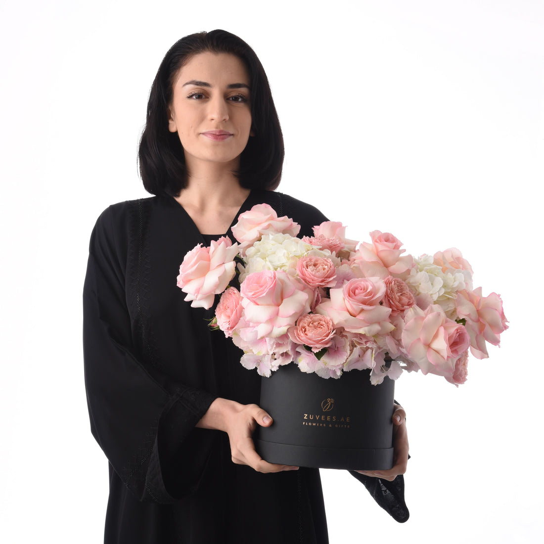 Elegant woman holds lush pink rose and hydrangea bouquet in matte black box.