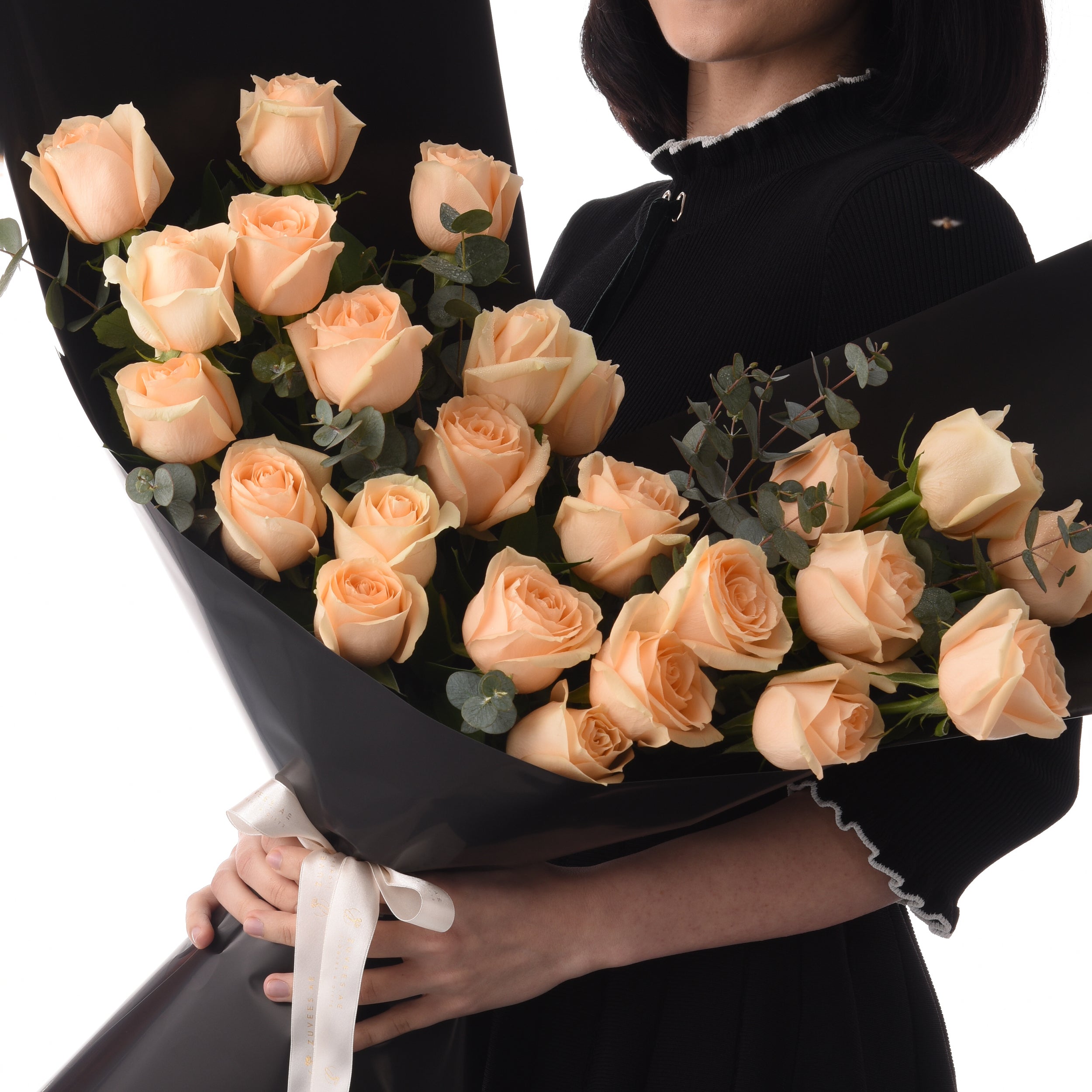 Soft peach roses in black wrap, held by person in black attire.