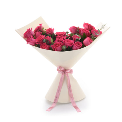 Vibrant pink roses in cream paper, tied with branded pink ribbon.