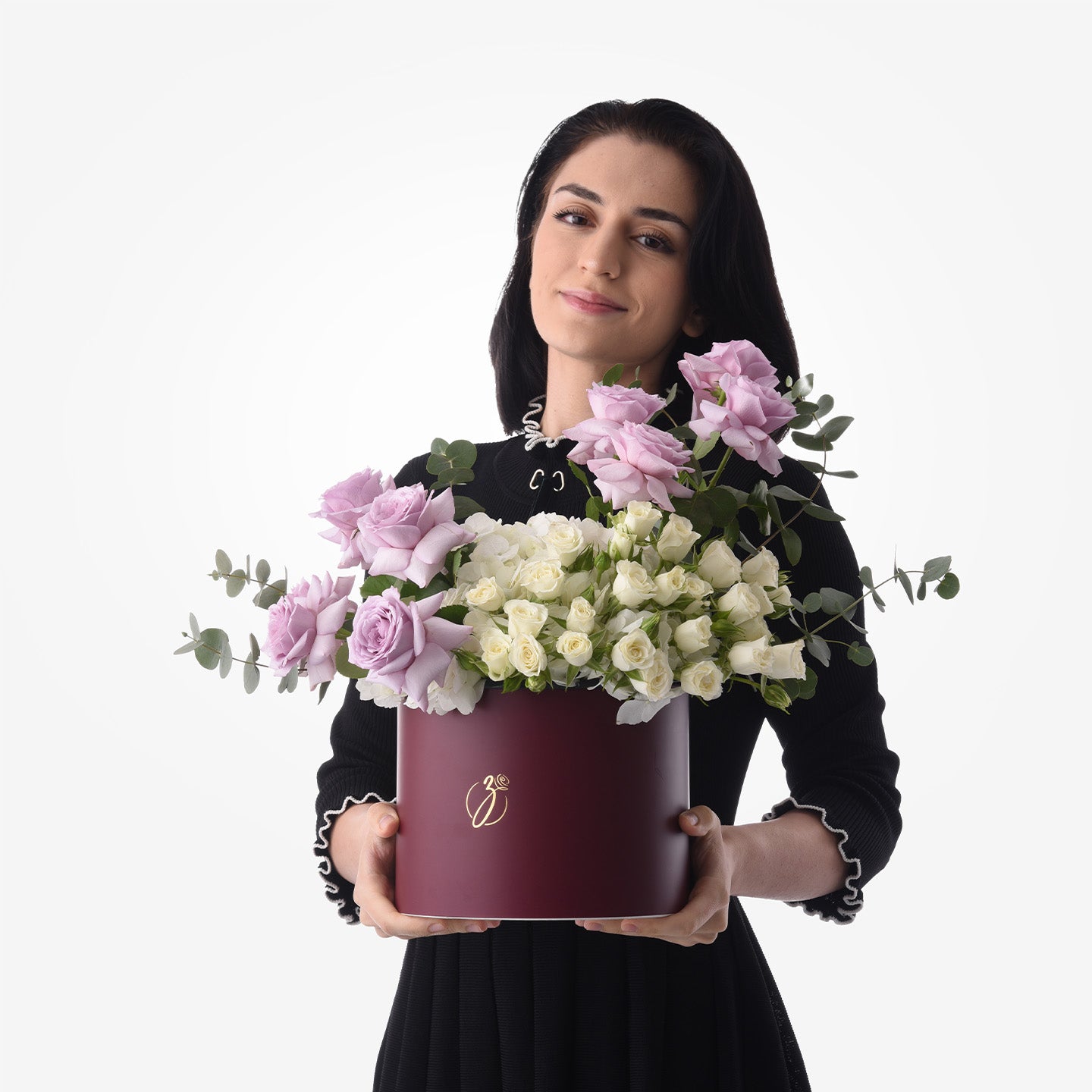 Elegant woman holds burgundy box with pink, white roses, green eucalyptus, gold logo.