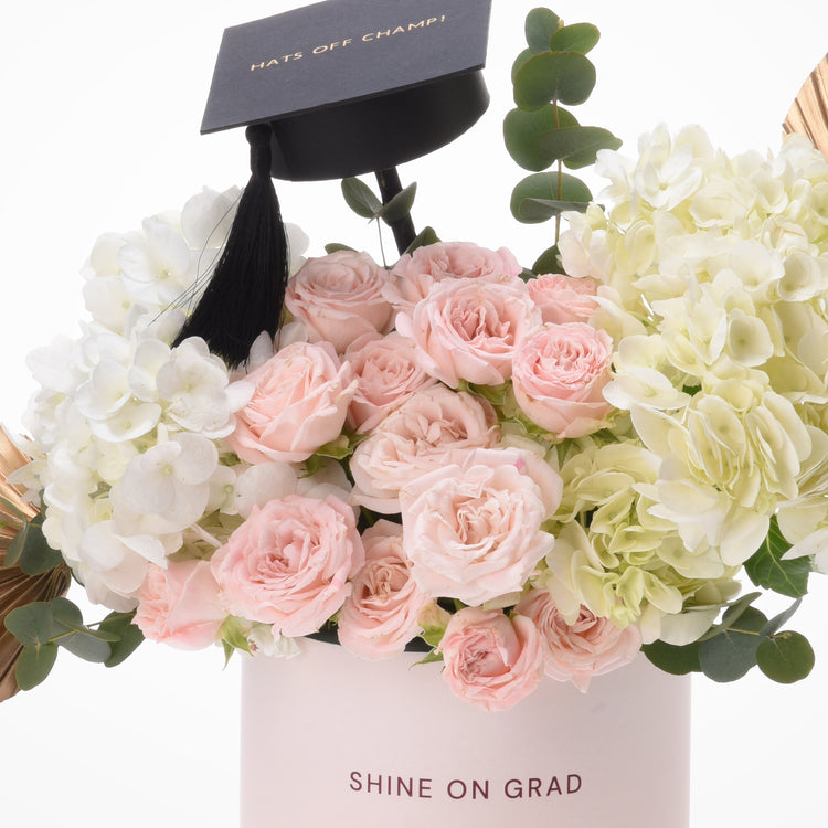 Pink roses and hydrangeas in graduation cap-themed floral arrangement.