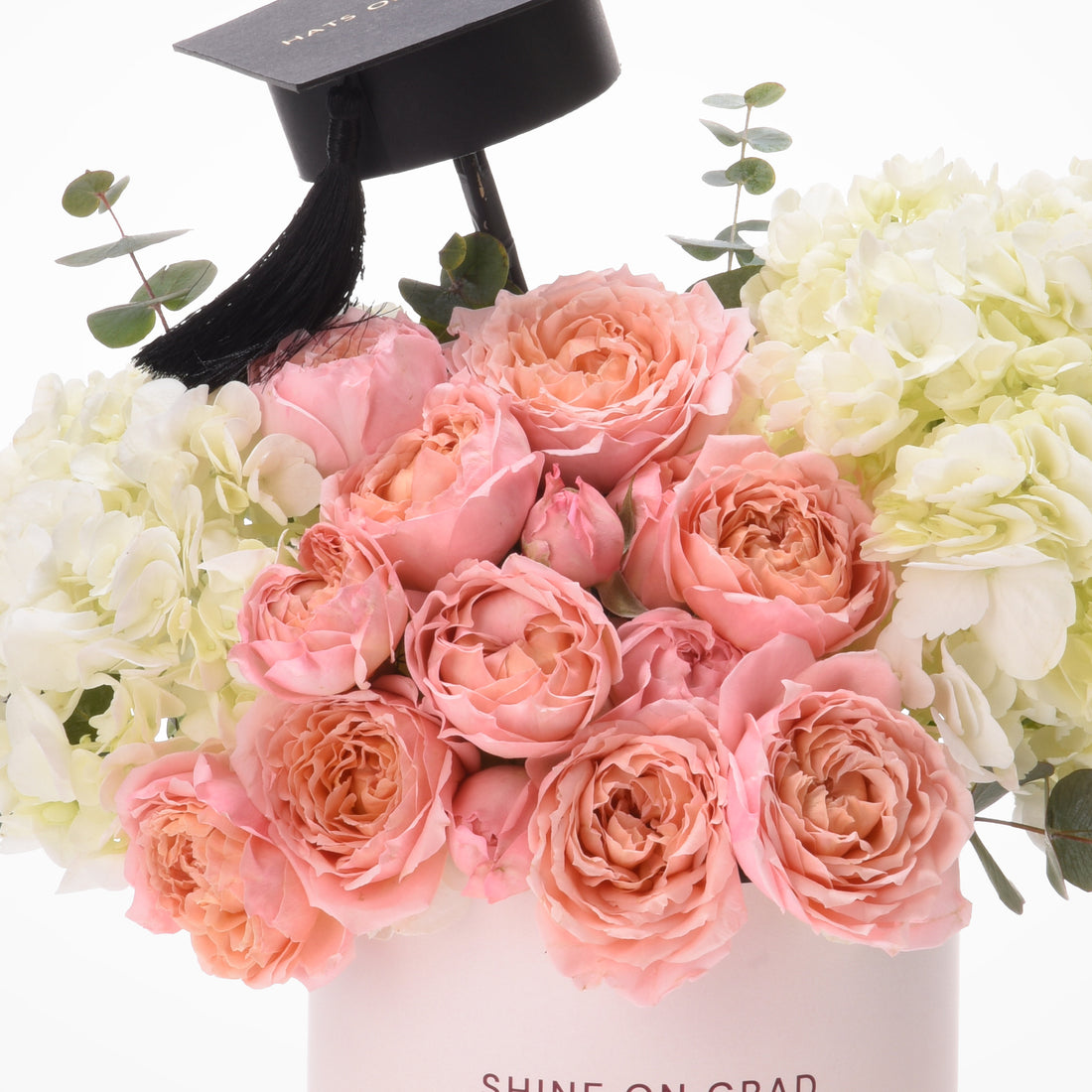 Pink roses, white hydrangeas, eucalyptus, black graduation cap in white box.