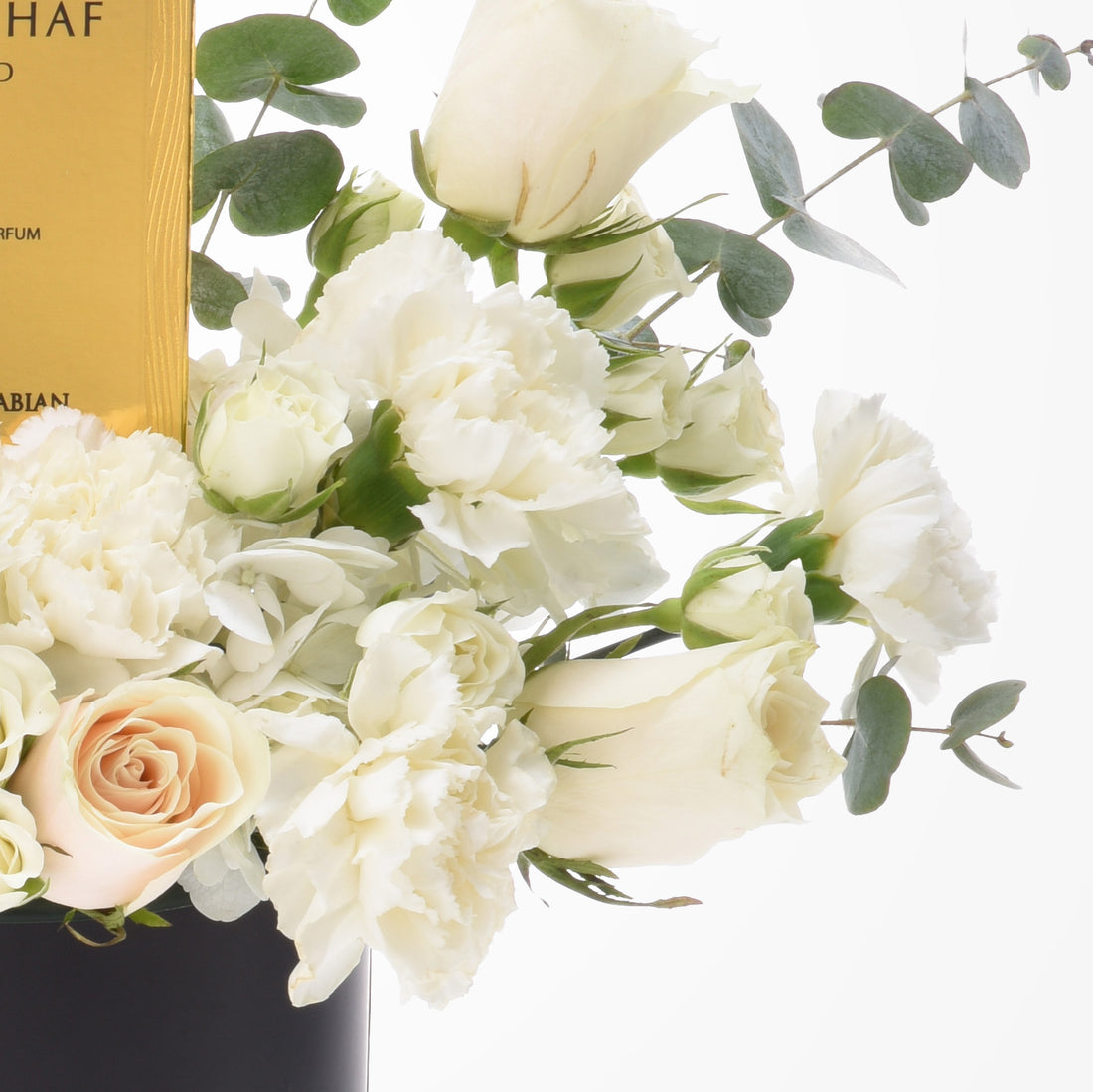 Elegant white roses and carnations with eucalyptus, beside gold perfume box.