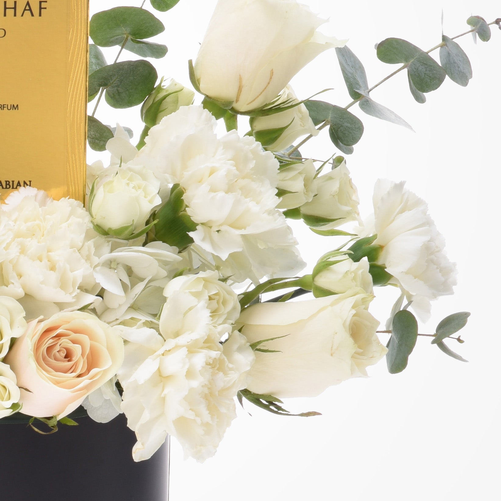 Elegant white roses and carnations with eucalyptus, beside gold perfume box.