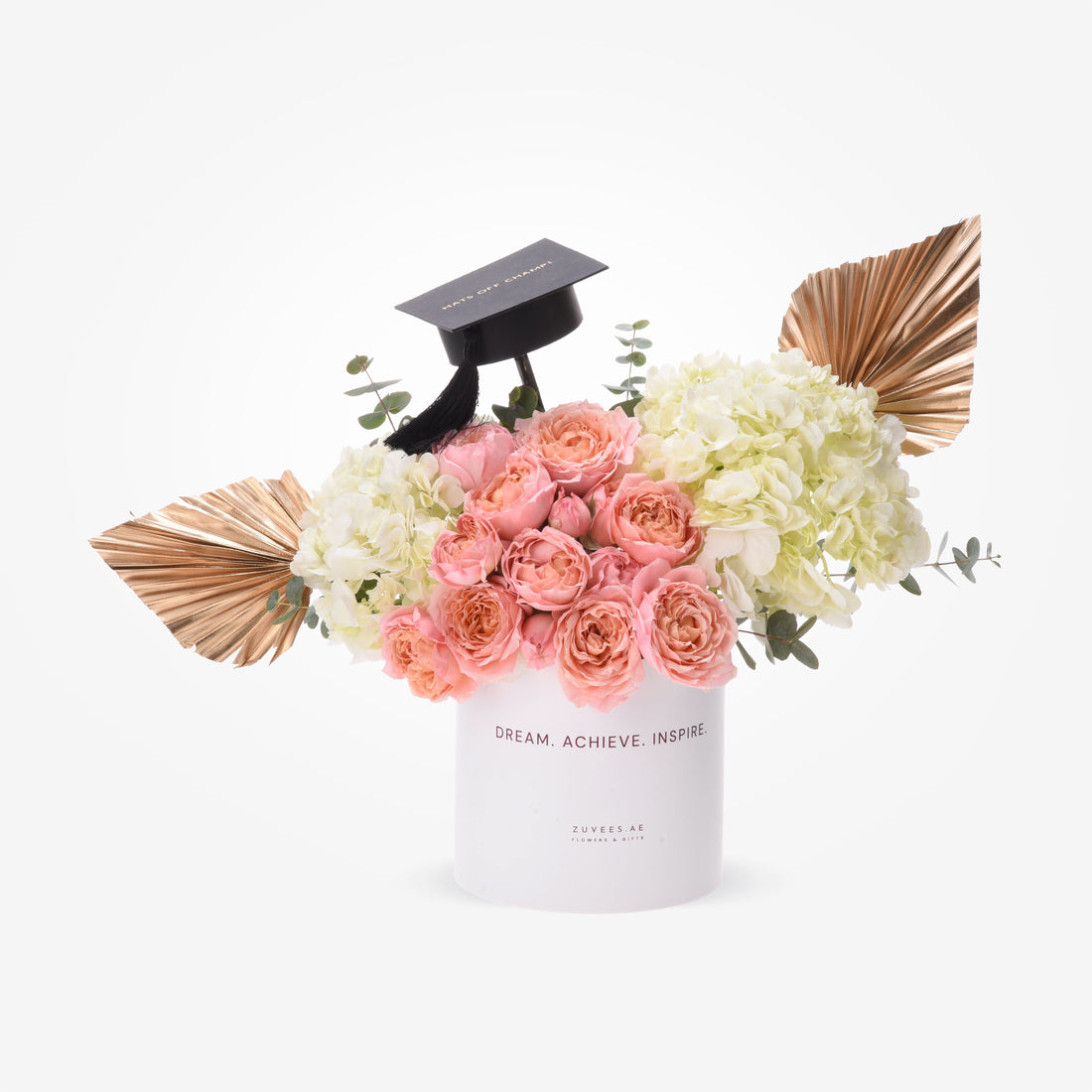 Pink roses, white hydrangeas, gold palms, and a black grad cap in a white "Dream. Achieve. Inspire." box.