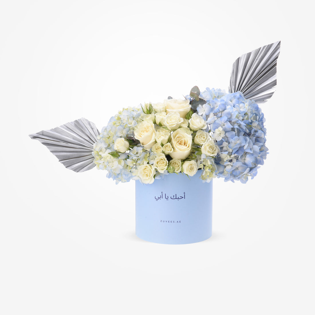 Elegant white roses, blue hydrangeas, silver leaves in light blue box with Arabic text.
