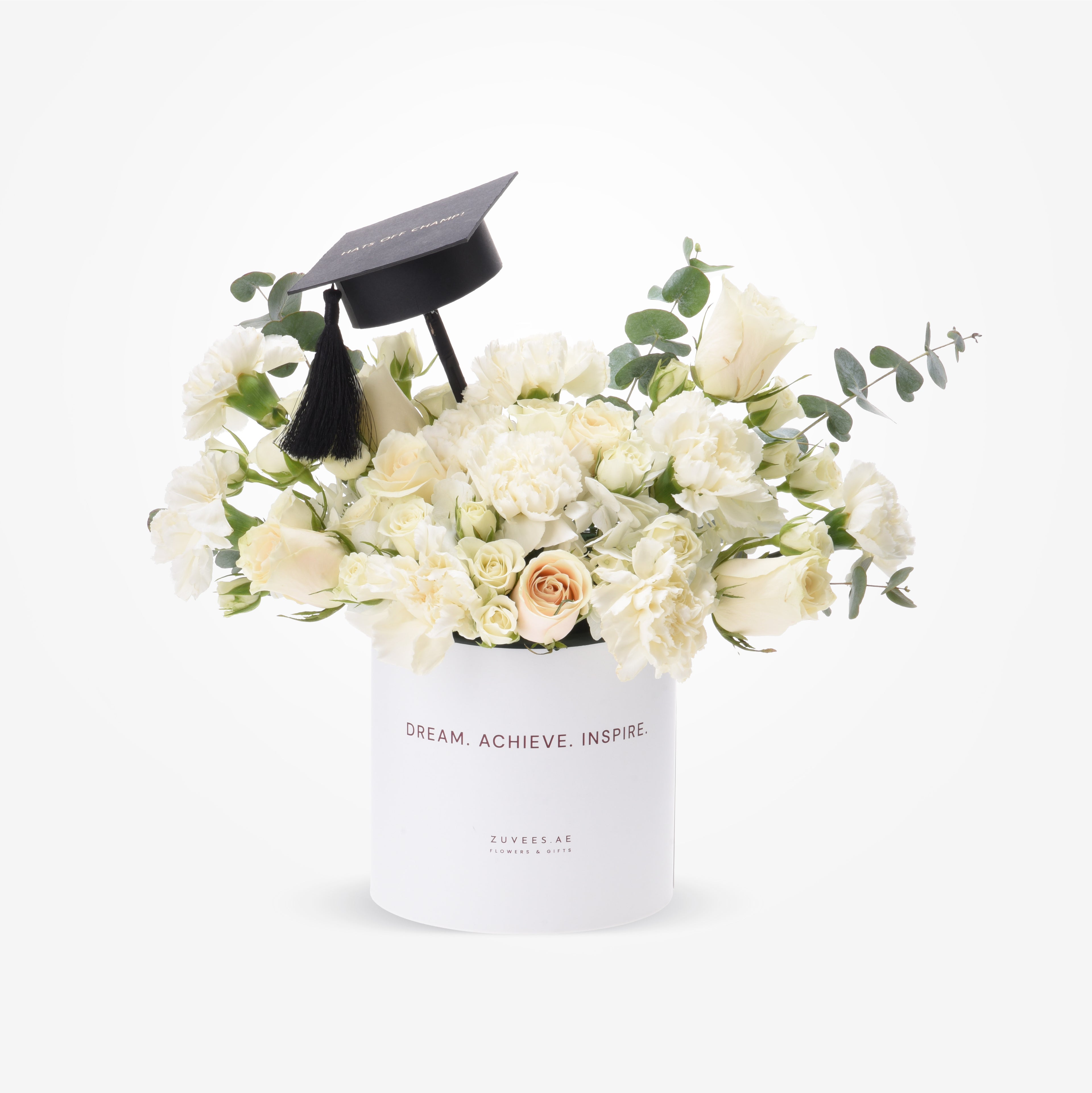 White roses and eucalyptus in sleek box topped with graduation cap.