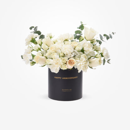 Elegant white roses and eucalyptus in black box with gold "Happy Anniversary" text.