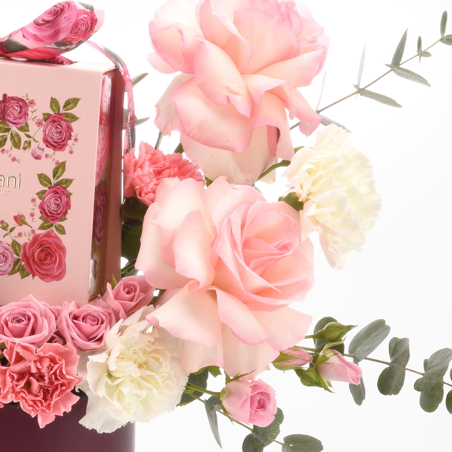 Soft pink roses and carnations elegantly arranged beside floral gift box.