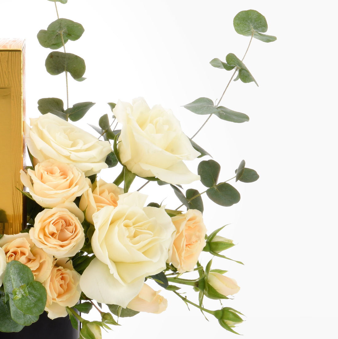 Cream and peach roses with eucalyptus, beside golden box, elegant floral arrangement.