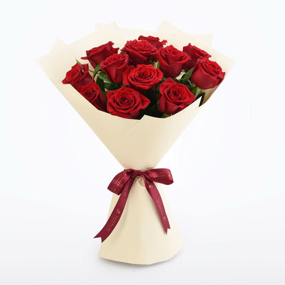 Vibrant red roses in cream paper, tied with burgundy ribbon.