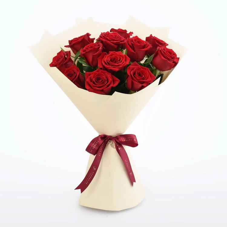 Vibrant red roses in cream paper, tied with burgundy ribbon.