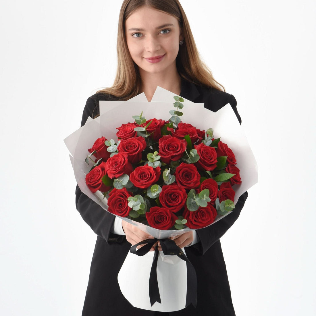 Woman holds vibrant red rose bouquet with eucalyptus, wrapped in white paper and black ribbon.