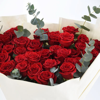 Vibrant red roses with dewdrops, accented by eucalyptus, wrapped in cream paper.