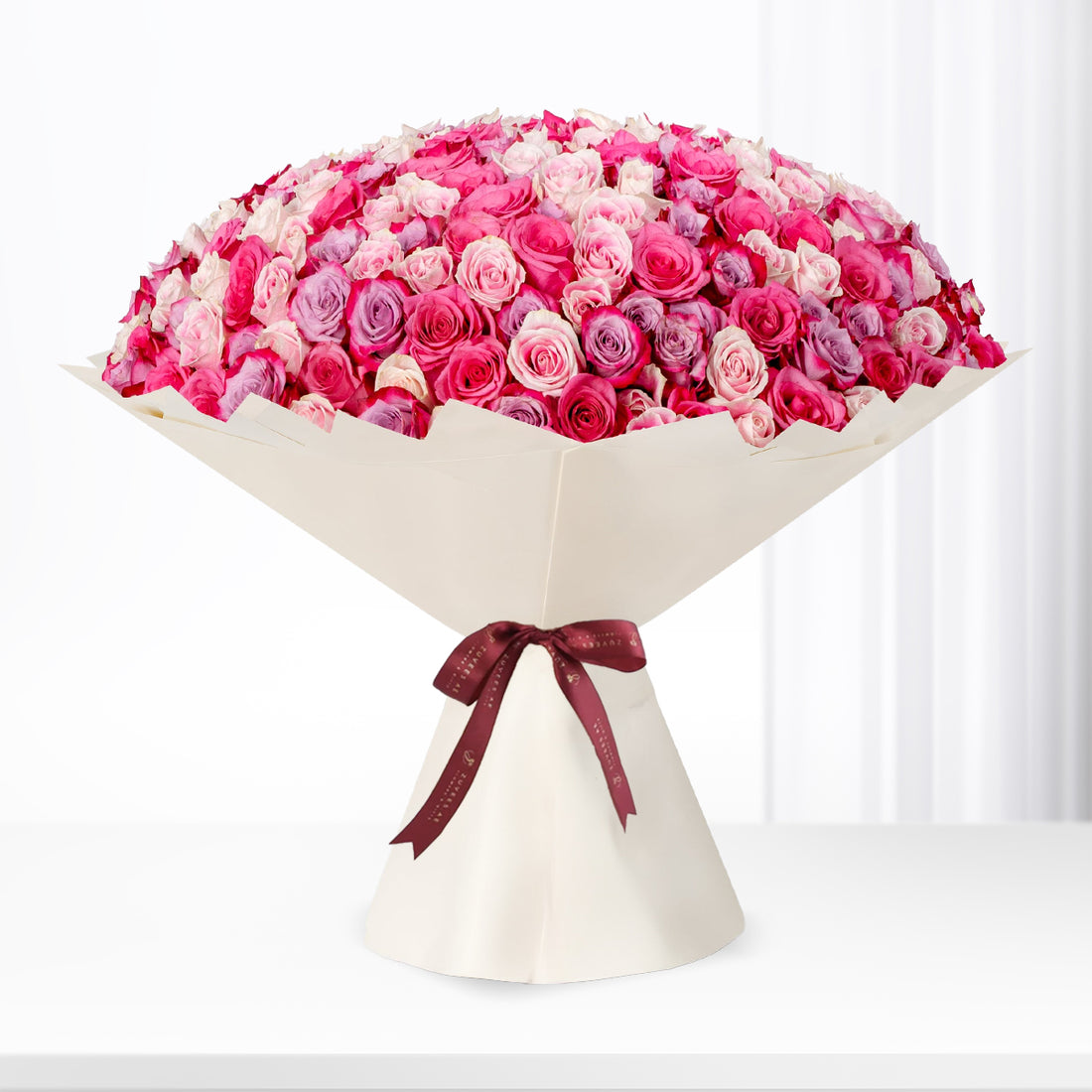 Vibrant pink and purple roses in cream paper, tied with burgundy ribbon.