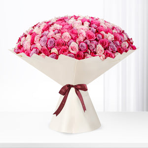 Vibrant pink and purple roses in cream paper, tied with burgundy ribbon.