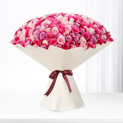 Vibrant pink and purple roses in cream paper, tied with burgundy ribbon.