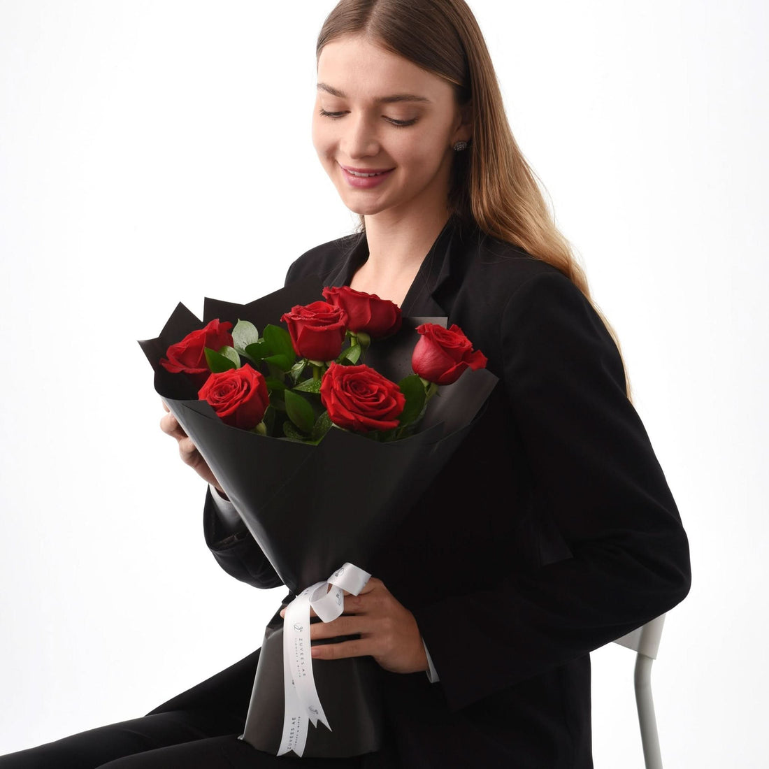 Woman in black suit holds elegant red rose bouquet wrapped in black paper with white ribbon.