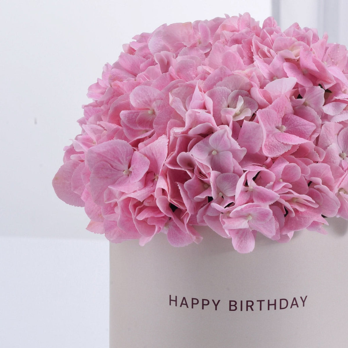Soft pink hydrangeas in minimalist white vase with "HAPPY BIRTHDAY" text.