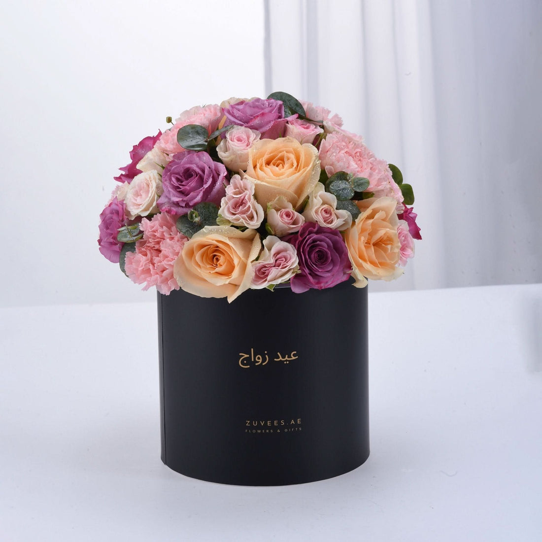 Elegant black box overflowing with blush, peach, and purple roses and carnations.