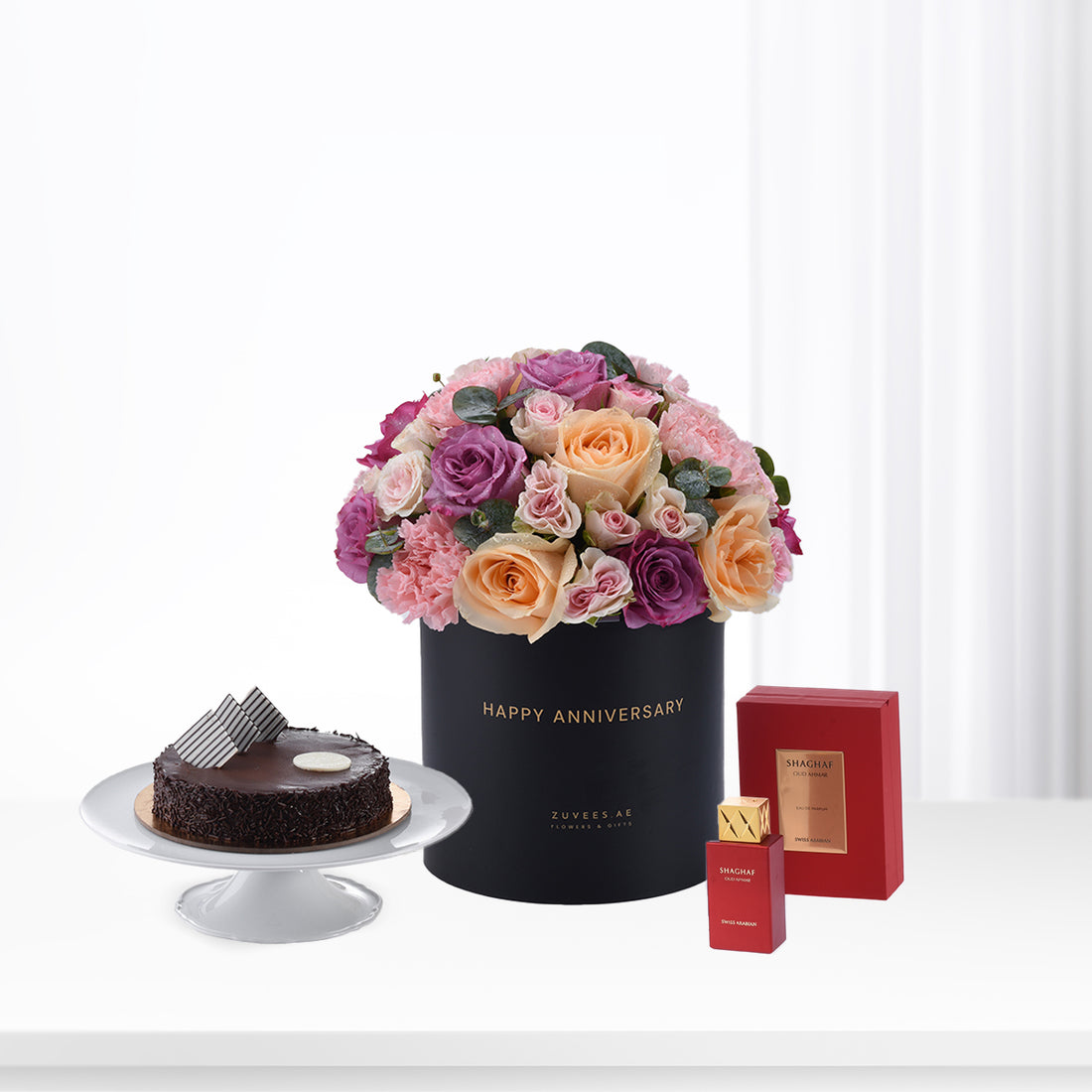 Luxurious anniversary gift set: roses, chocolate cake, and red perfume.