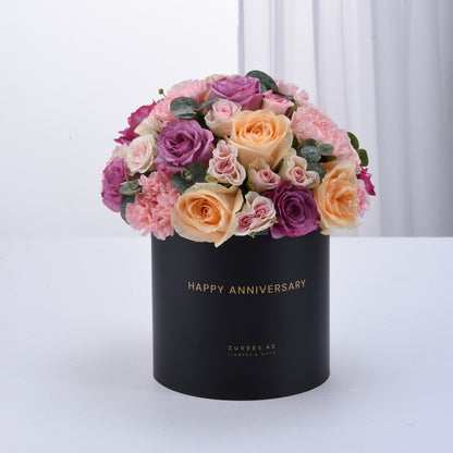 Black box holds vibrant pink, purple, and peach roses with "Happy Anniversary" gold text.
