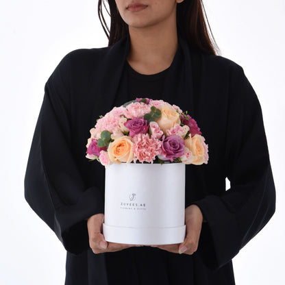 Elegant white hat box filled with soft pink, peach, and purple roses and carnations.