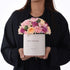 White box holds vibrant pink, purple, peach roses and carnations for birthday.